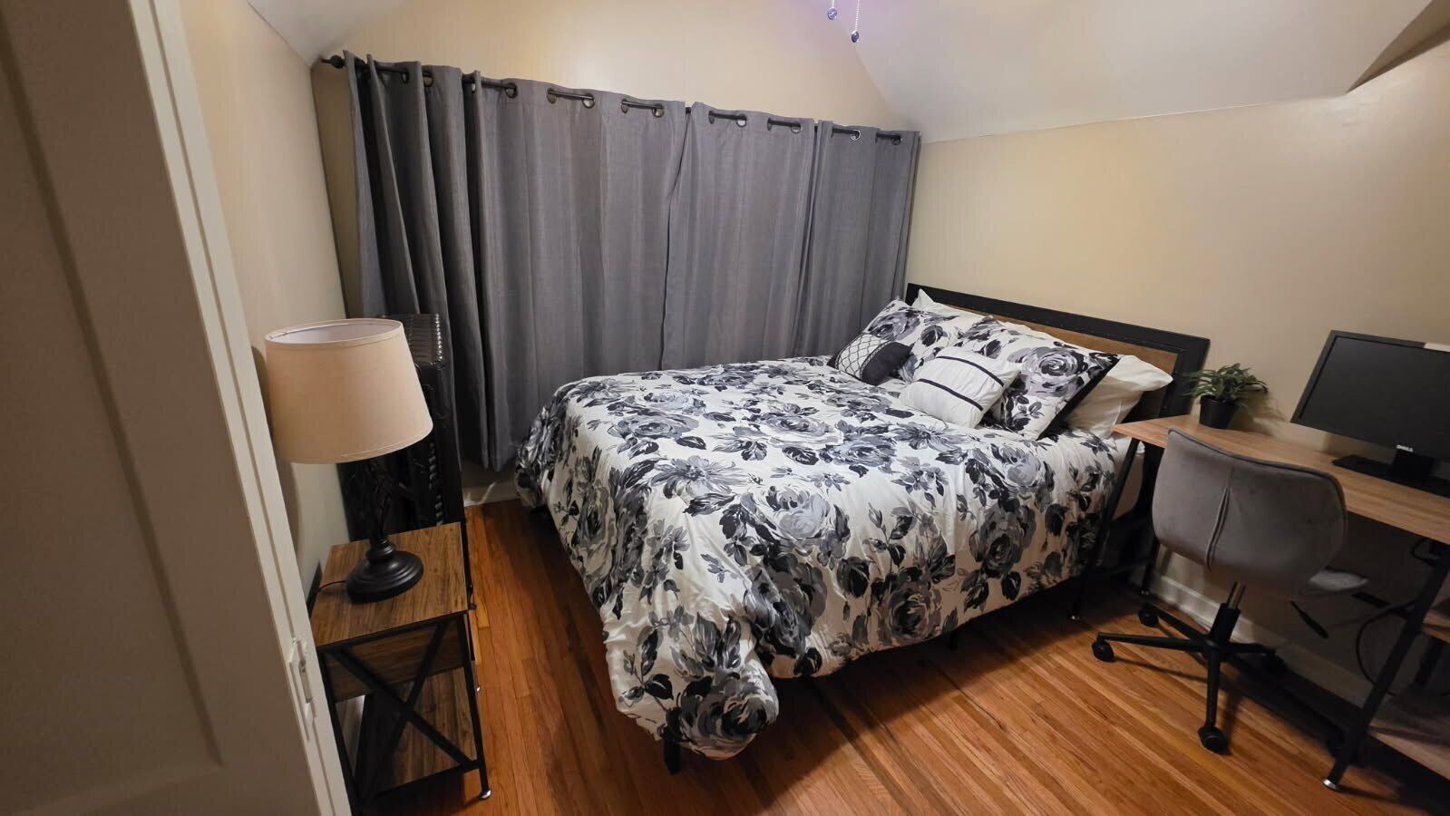 Un dormitorio con una cama, un escritorio, una silla, una lámpara y una cortina.