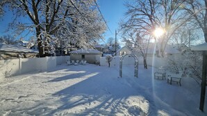 A snow-covered backyard with a patio area, a small shed, and a tree. - 4BR NE Minneapolis Home - Sleeps 10, Workspaces, Fenced Yard & EV Charging (Minneapolis)