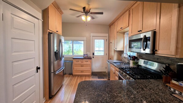 A kitchen with wooden cabinets, stainless steel appliances, granite countertops, and a ceiling fan.