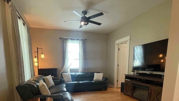A living room with a sofa, a coffee table, a TV, and a ceiling fan. - 4BR NE Minneapolis Home - Sleeps 10, Workspaces, Fenced Yard & EV Charging (Minneapolis)
