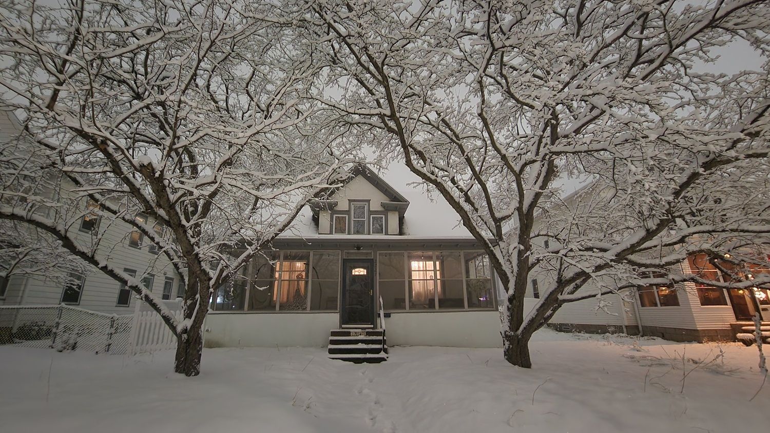A two-story house with a front porch and a snow-covered yard.
