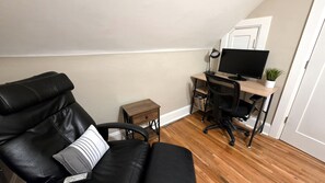 Une pièce comprenant un canapé en cuir noir, un bureau en bois avec un ordinateur et une petite table d’appoint en bois.
