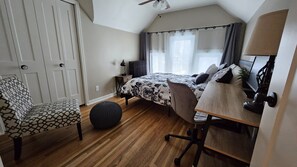 A bedroom with a bed, a desk, a chair, a radiator, and a window with curtains.