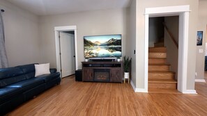 A living room with a flat-screen TV, a dark leather sofa, wooden flooring, and a staircase leading to another level.