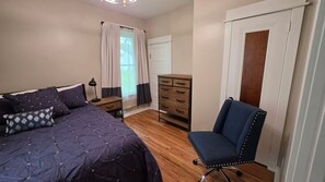Une chambre à coucher avec un lit, une commode, une chaise et une fenêtre avec des rideaux.