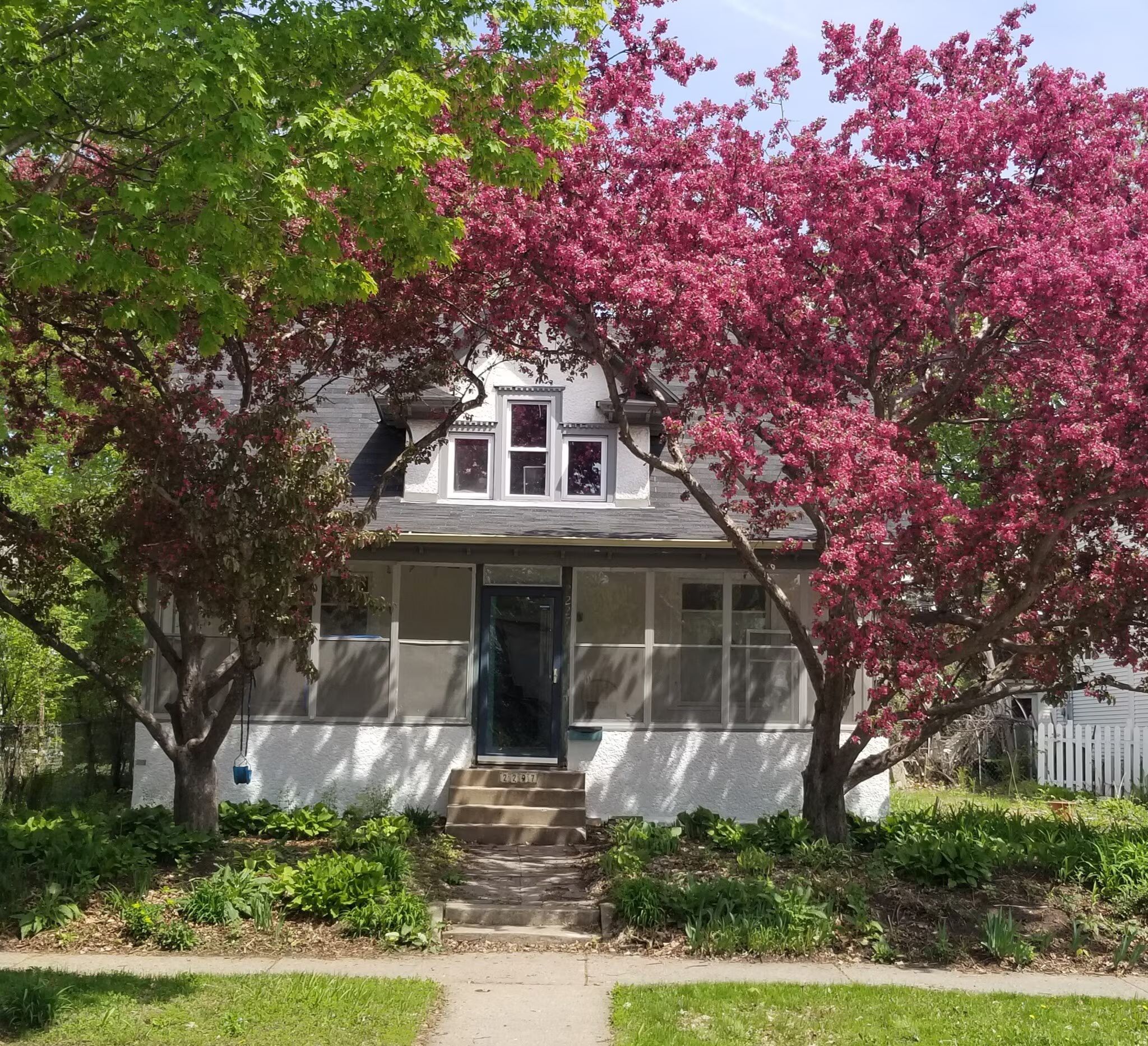 A two-story house with a front porch, a visible front door, and a small staircase leading to the entrance.