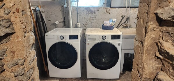 Deux lave-linge à chargement frontal blancs de la marque LG ThinQ, dans une buanderie aux murs en pierre et dotée d’une fenêtre.