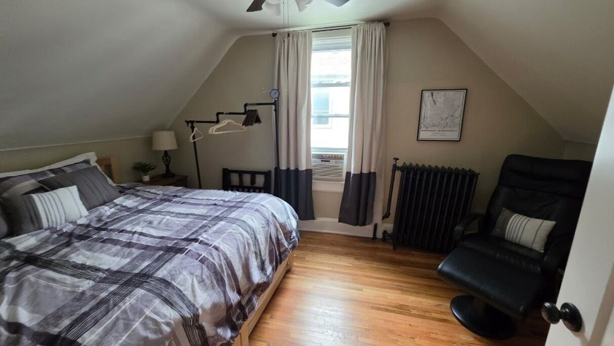 Une chambre à coucher avec un lit, une chaise, un radiateur et une fenêtre avec des rideaux.