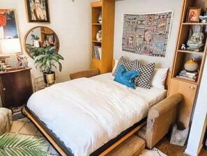Cozy retreat with a single bed, bookshelf, mirror, and potted plant.