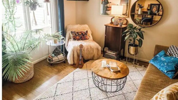 A cozy living room with a sofa, a coffee table, and a guitar. There are potted plants, a TV, and artwork on the walls. - Cape Fear’s Original 1908 Cozy Historic Getaway (Wilmington)