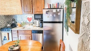 A kitchen with wooden cabinets, a stainless steel refrigerator, a microwave, and a stove. There is a dining table with chairs and a plant on it. - Cape Fear’s Original 1908 Cozy Historic Getaway (Wilmington)