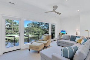 Relax in this stylish living room with a large sectional sofa, armchair, and ottoman, perfect for unwinding with a view of the surrounding landscape.