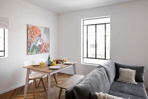A modern living room with a grey sofa, a wooden dining table, and a colorful abstract painting on the wall.