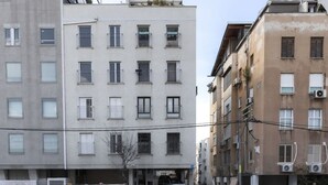 A multi-story residential building with balconies, a gated entrance, and parked cars.