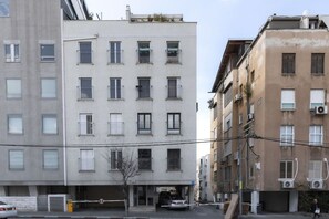 A multi-story residential building with balconies, a gated entrance, and parked cars.