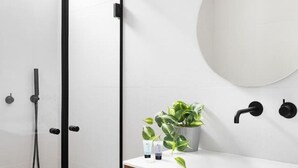 A modern bathroom with a glass shower enclosure, a wooden vanity, a round mirror, and a potted plant.