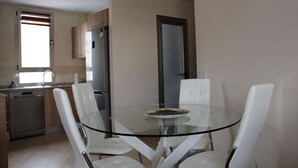Una cocina moderna con una mesa de comedor de vidrio y sillas blancas, un refrigerador de acero inoxidable y armarios de madera.