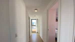A narrow hallway with white walls and a tiled floor leading to a bedroom with a bed and a pink wall. - PLAZA MAYOR - Apartment with beautiful sea and rock views (Calpe / Calp)