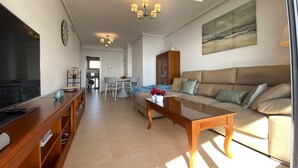 A modern living room with a sofa, coffee table, and dining area. There is a kitchen in the background with a washing machine and a dining table. - PLAZA MAYOR - Apartment with beautiful sea and rock views (Calpe / Calp)