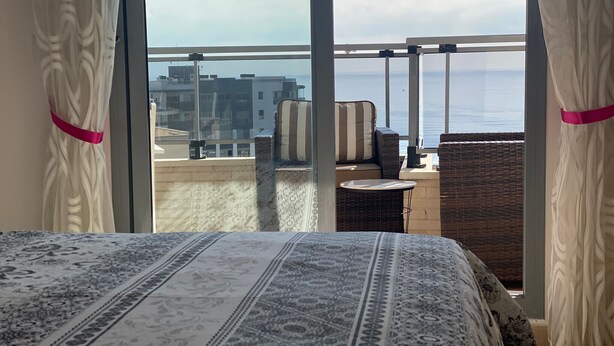 A balcony with a bed, wicker furniture, and a view of the sea and buildings. - PLAZA MAYOR - Apartment with beautiful sea and rock views (Calpe / Calp)