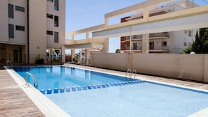 A rectangular swimming pool with a wooden deck and metal handrails, surrounded by a low wall and adjacent buildings. - PLAZA MAYOR - Apartment with beautiful sea and rock views (Calpe / Calp)