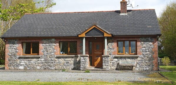 A stone building with a dark tiled roof, a wooden front door, and two windows on the ground floor. - Cottage on Lough Ree / River Shannon in the heart of Ireland (Newtowncashel)