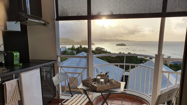 A balcony with a view of the sea, a small table with a tray, and a white refrigerator.