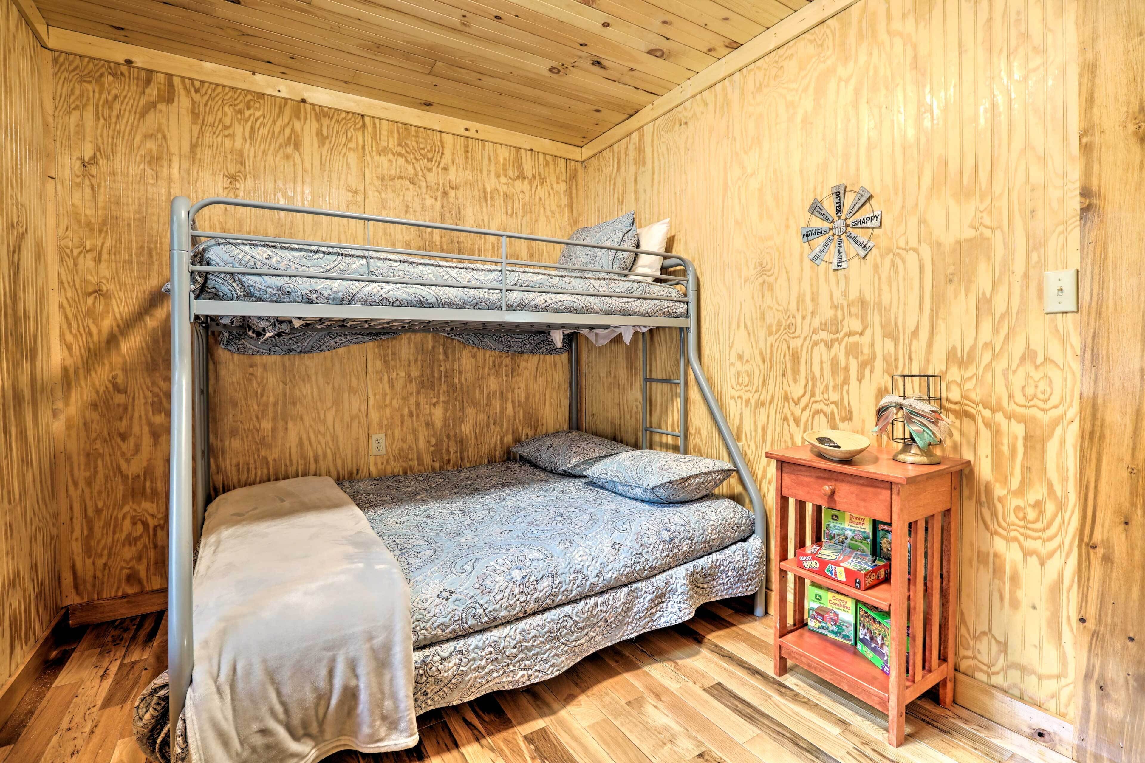 A bunk bed with a patterned bedspread and pillows, a small wooden nightstand with books, and a wall clock.