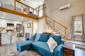 A modern living space with a blue sectional sofa, a wooden staircase, and a kitchen area. - West Atlanta Craftsman Studio with Front Yard! (Atlanta)