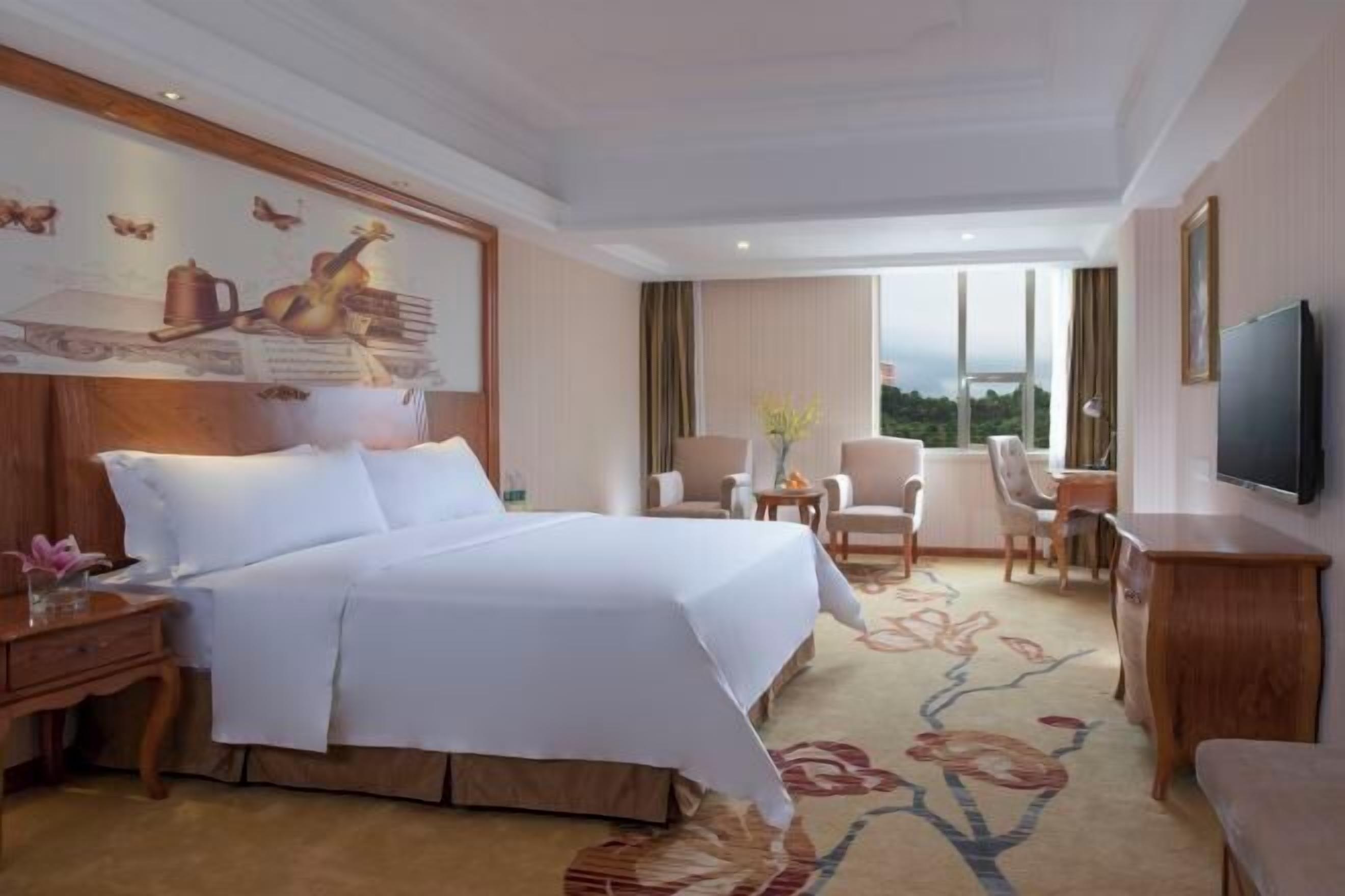 A hotel room with a large bed, a television, a desk, and a view of the outdoors.