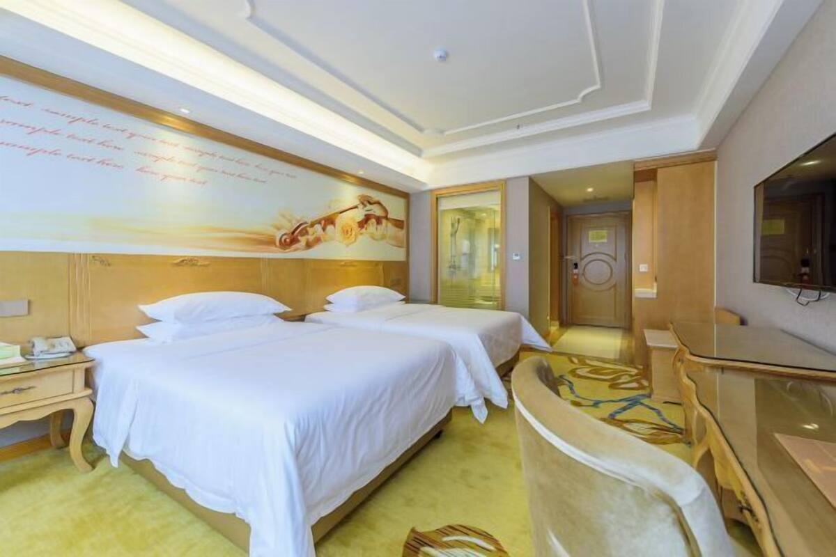 A hotel room with two beds, a desk, a television, and a wall with a decorative mural.
