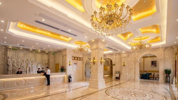 A spacious lobby with a reception desk, chandeliers, and a large decorative floor pattern.