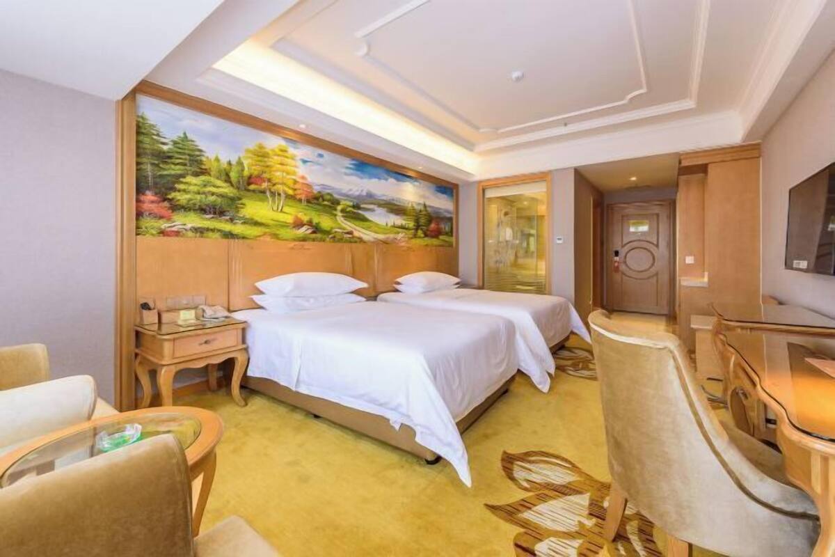 A hotel room with a large bed, a desk, a chair, and a painting on the wall.
