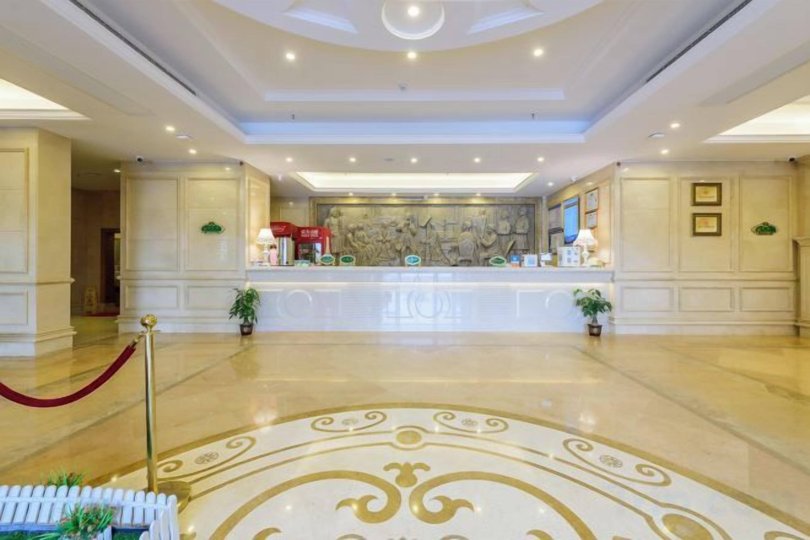 A spacious lobby with a reception desk, potted plants, and a marble floor.