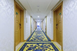 Een lange gang met deuren aan beide kanten, een kamerbreed tapijt en een plafond met ingebouwde verlichting.