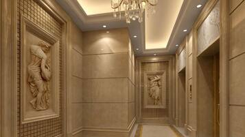 A hallway with marble walls, a chandelier, and classical sculptures.