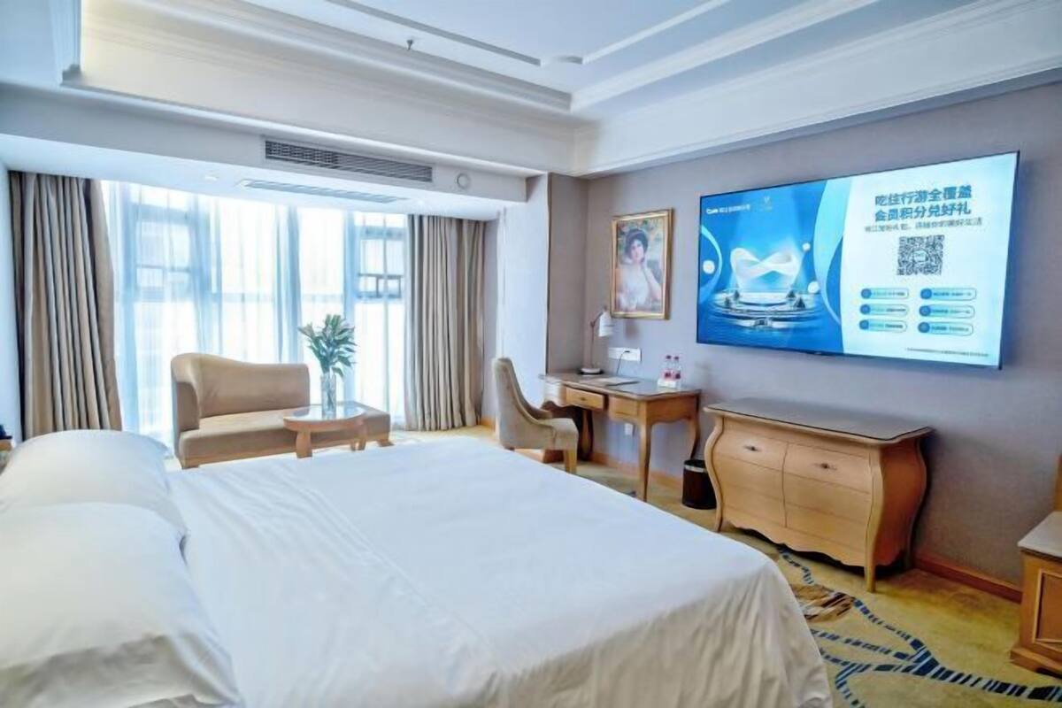 A hotel room with a large bed, a desk, a chair, and a television on the wall.
