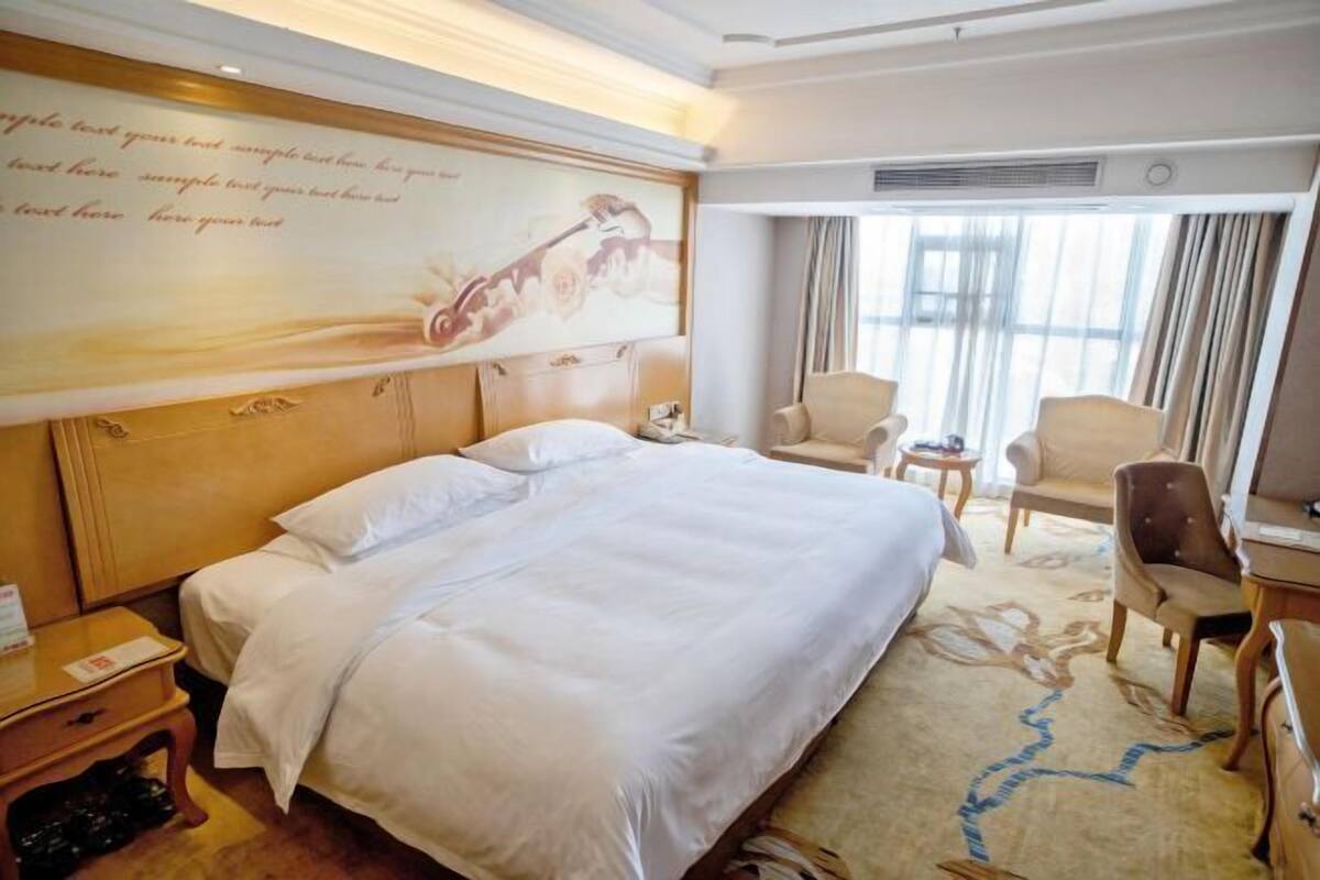 A hotel room with a large bed, a desk, a chair, and a window with curtains.