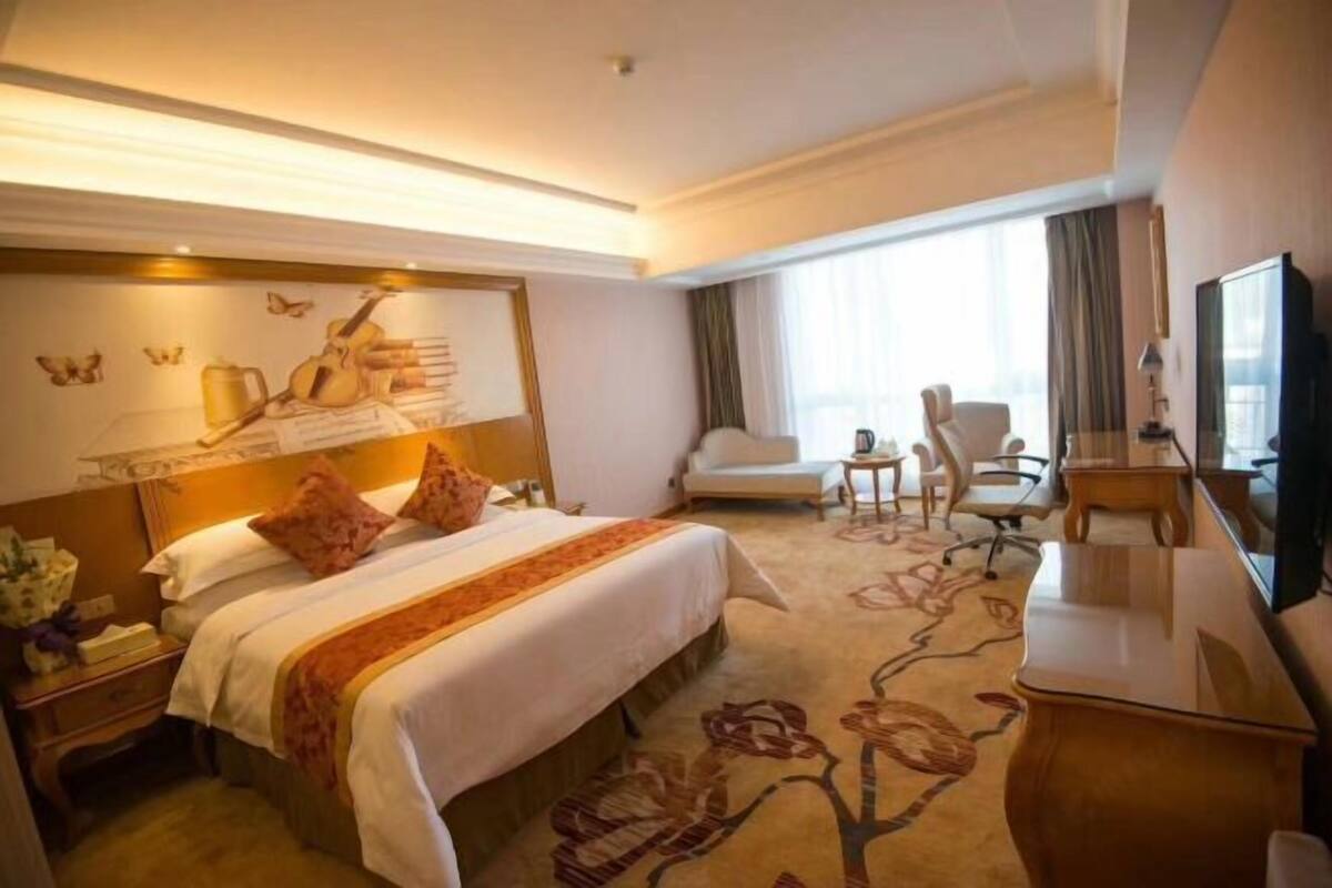 A hotel room with a large bed, a desk, a chair, and a television.