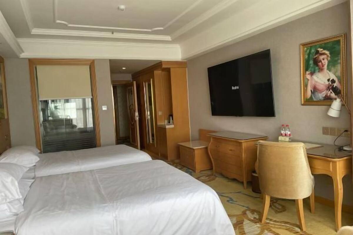 A hotel room with two beds, a desk, a chair, a television, and a painting on the wall.