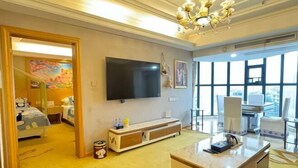 A hotel room with a large TV, a console table, a sofa, a desk, and a large window.