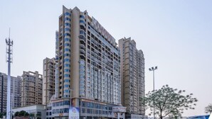 A high-rise residential building with multiple balconies, a ground-level commercial area, and a clear sky.