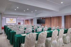 A conference room with rows of tables and chairs, a podium, and a screen. - Vienna International Hotel (Beihai Hepu Hesi Shougang Branch) (Hepu)
