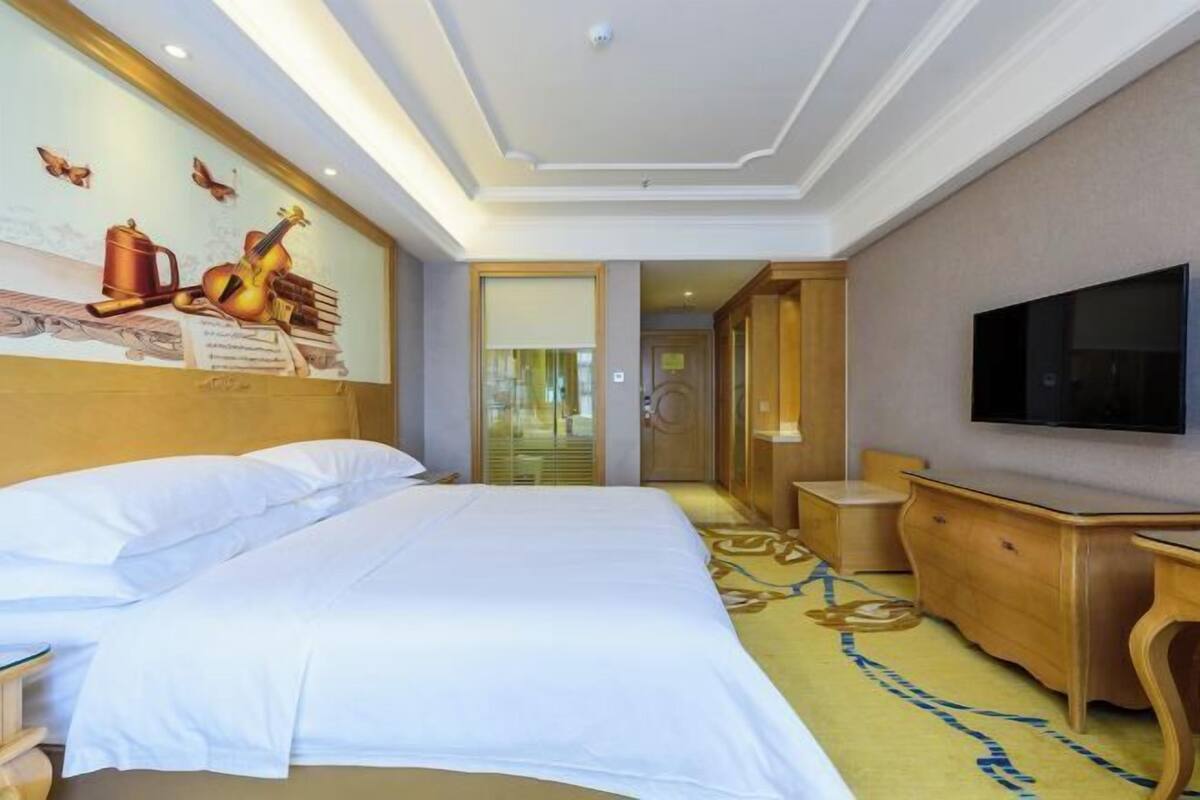 A hotel room with a large bed, a television, a desk, and a wall-mounted TV.