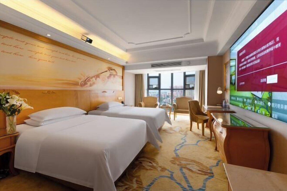 Une chambre d’hôtel avec deux lits, une grande fenêtre, un téléviseur et un mur décoratif.