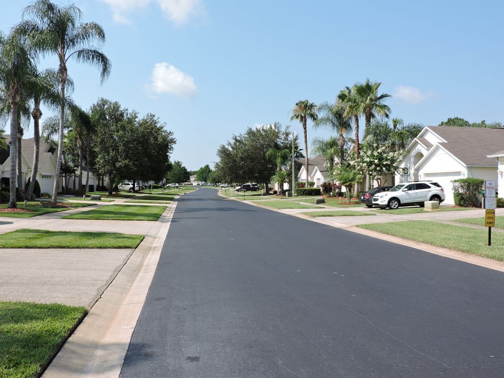 Una calle residencial con casas, palmeras y cielo despejado.
