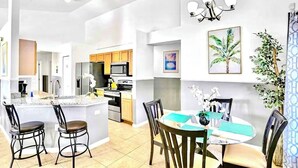 Una cocina moderna con armarios blancos, una isla central con taburetes y una zona de comedor con una mesa redonda y sillas.
