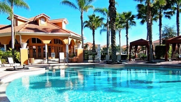 Une piscine à l’eau d’un bleu cristallin, entourée de palmiers et bordée d’un bâtiment dont le toit est recouvert de tuiles.