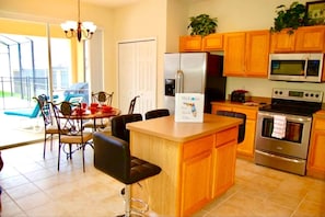 Een moderne keuken met houten kastjes, een roestvrijstalen koelkast, een magnetron en een oven. Er is een eethoek met een tafel en stoelen, en een bordje met de tekst 'Welcome to Florida Villas'.