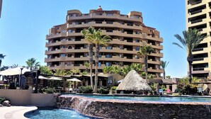 Un resort con piscina, palmeras y un edificio de varios pisos con balcones.